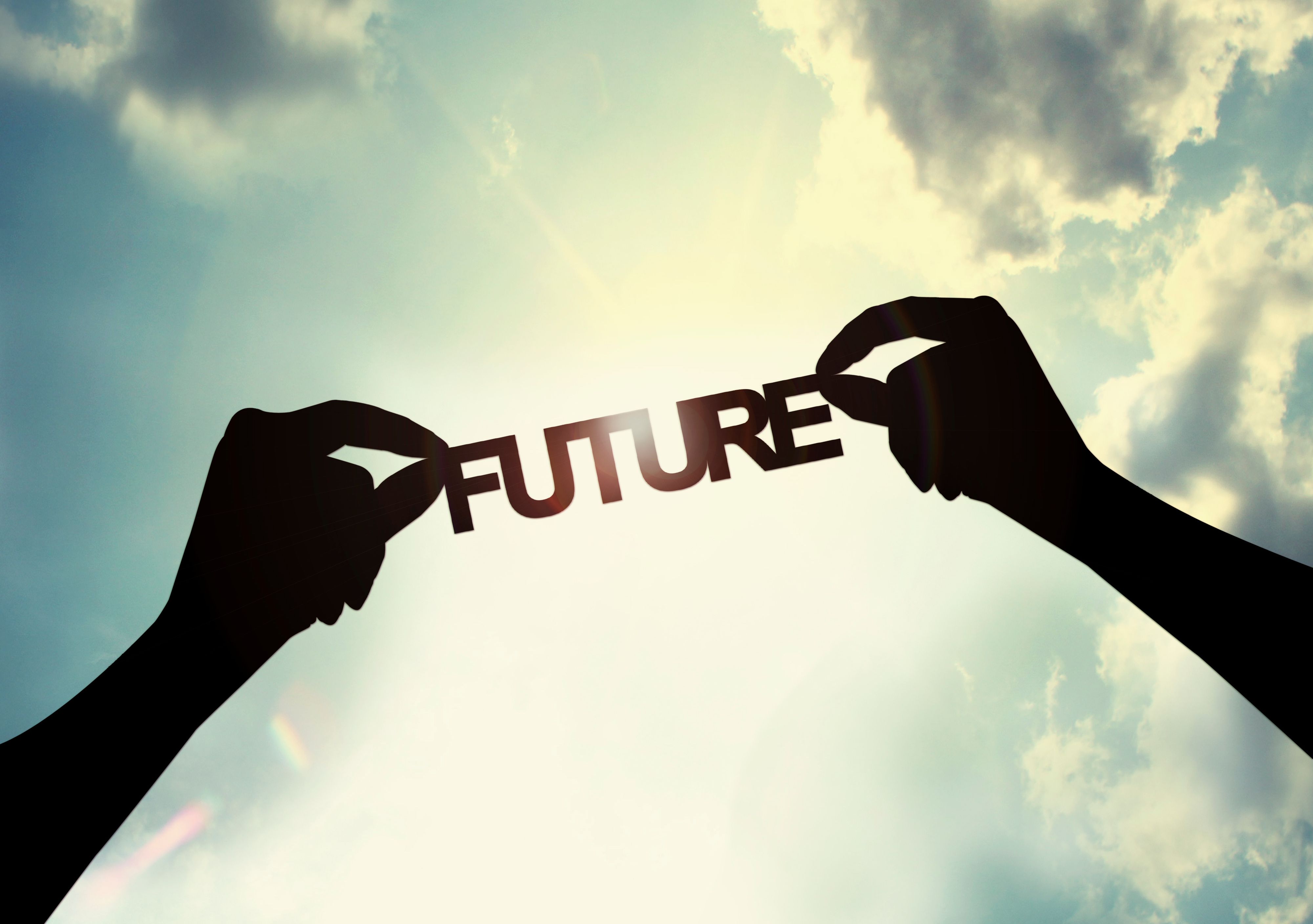 Zwei Hände halten den Schriftzug "Future" in Richtung Himmel. Der Himmel ist blau mit einzelnen Wolken und die strahlende Sonne ist deutlich sichtbar.